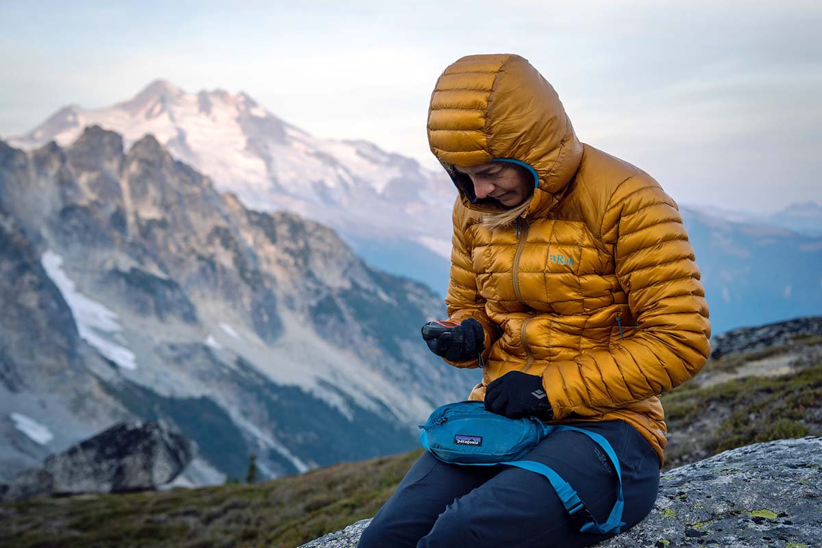 Sitting on rock using Garmin inReach Mini 2 (women's down jackets)